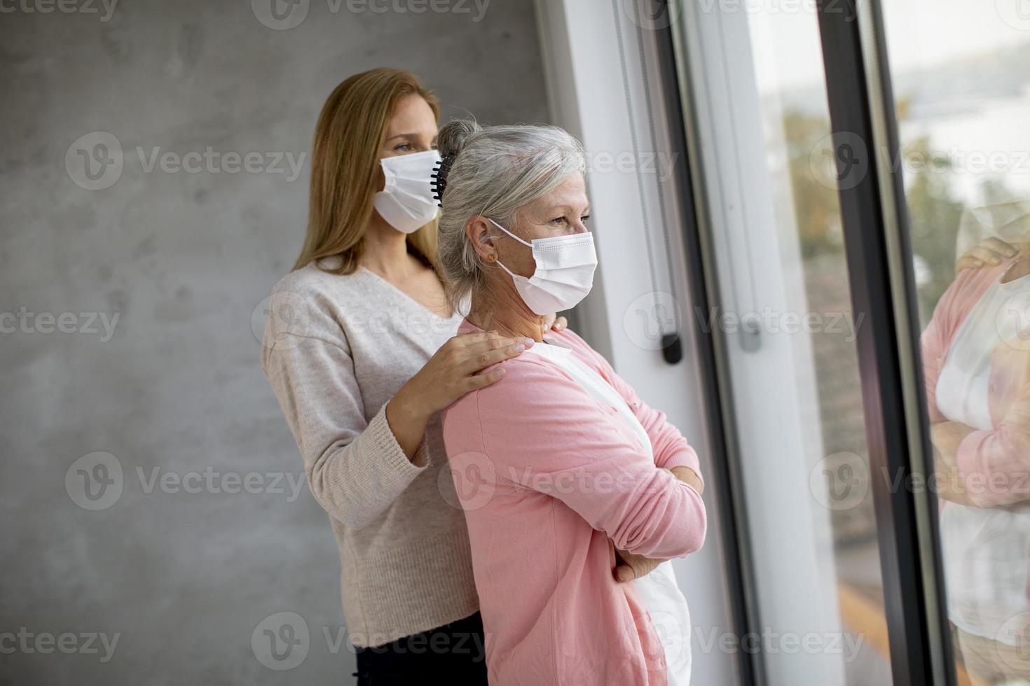 volwassen moeder en dochter kijkt uit raam met maskers op foto