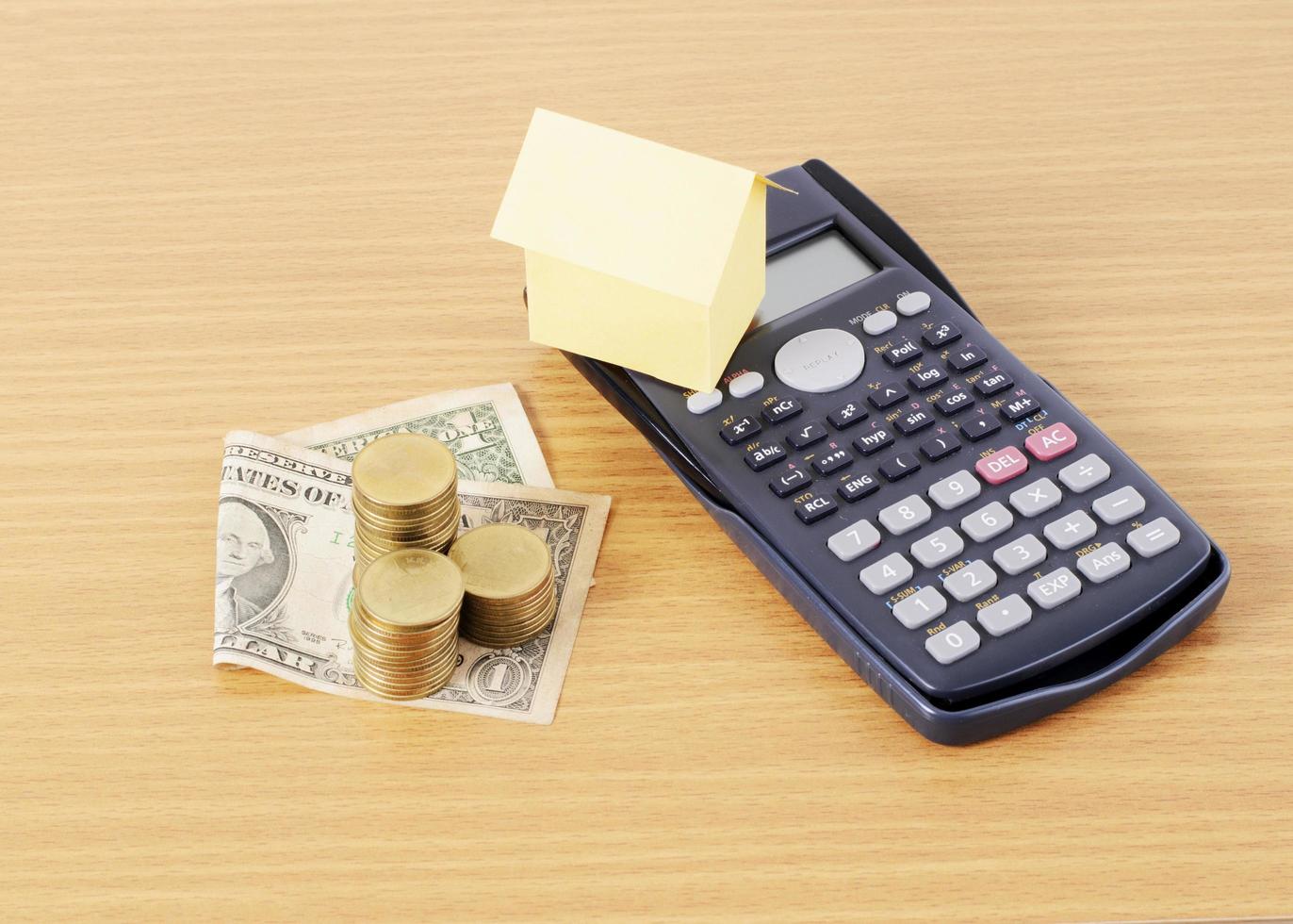 calculator en huisdocument met dollargeld en muntstukkenstapel op houten bureau voor leningenconcept foto