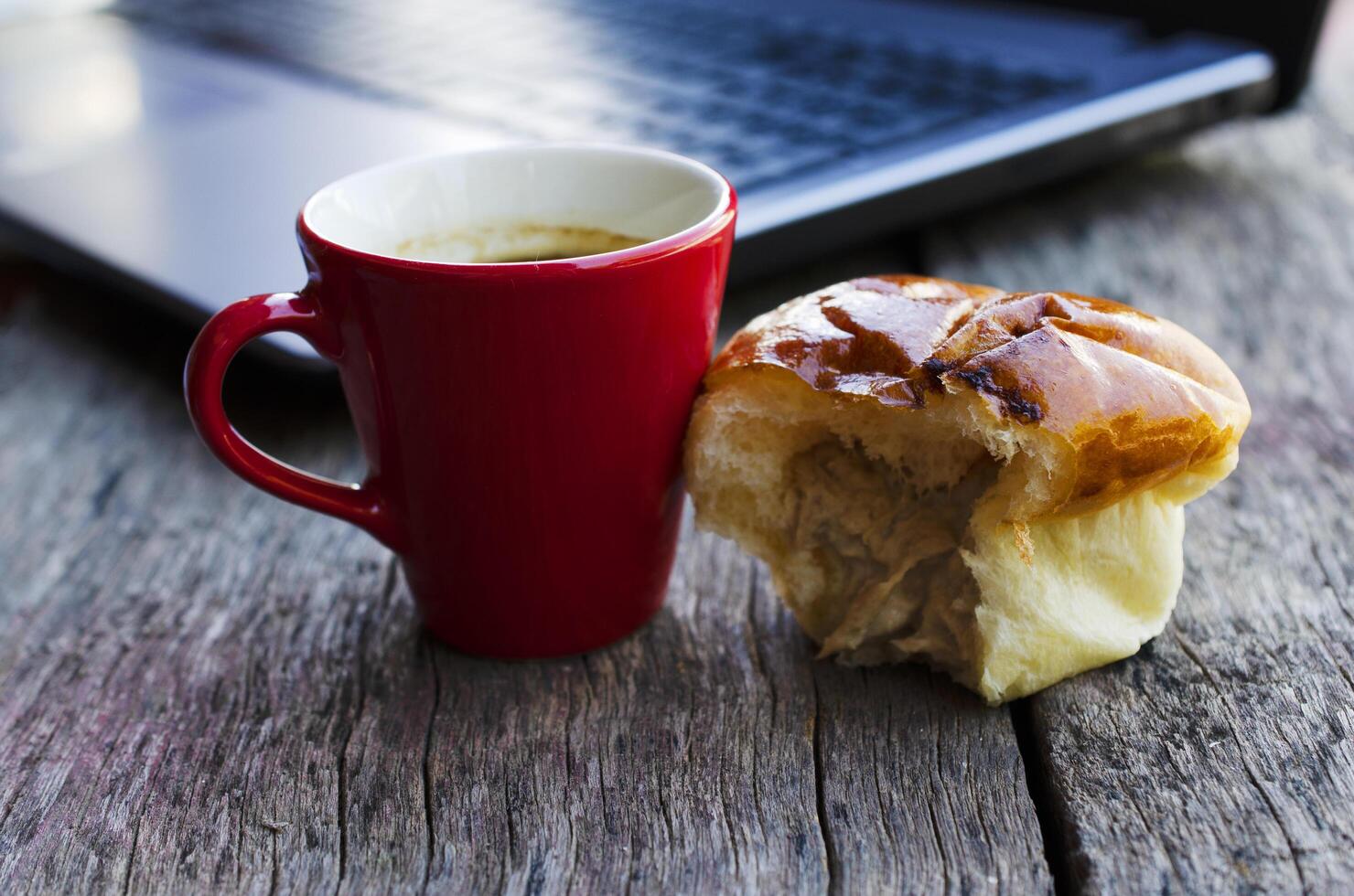 rode koffiekopje en tonijnbroodje brood met laptop op houten tafel voor lifestyle technologie digitale nomade foto