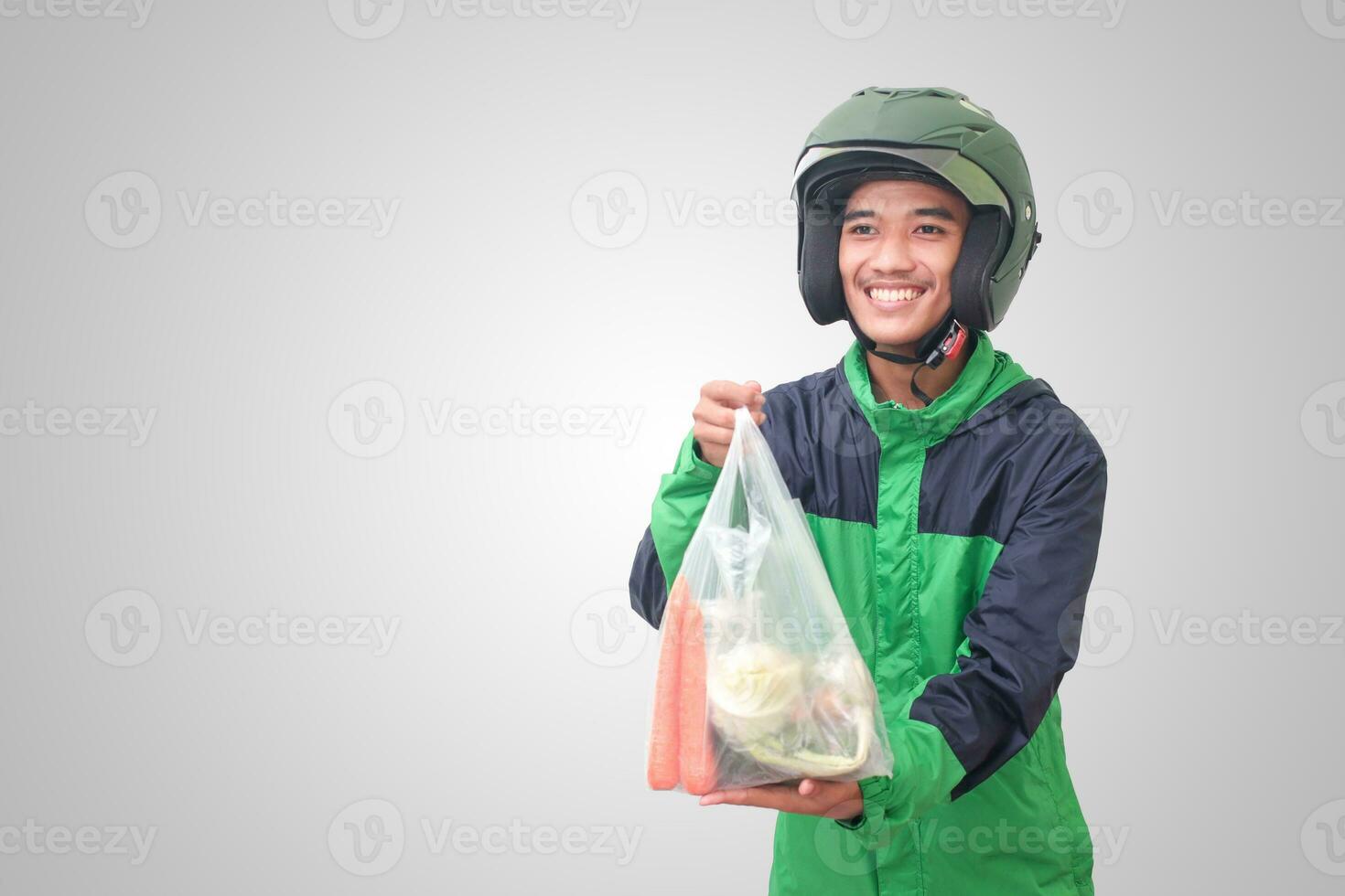 portret van Aziatisch online taxi bestuurder vervelend groen jasje en helm leveren de groenten van traditioneel markt en richten met vinger. geïsoleerd beeld Aan wit achtergrond foto