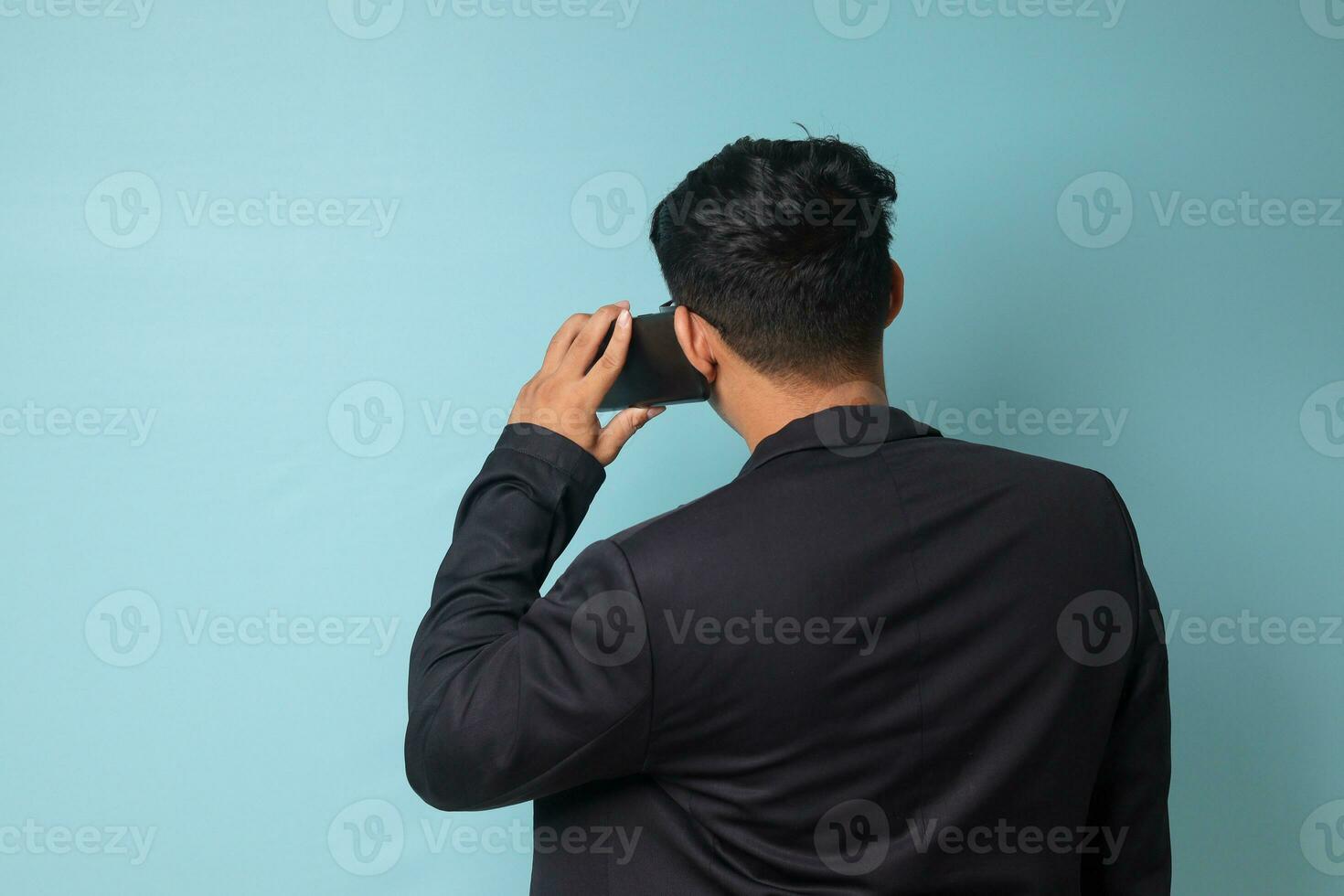 portret van jong Aziatisch bedrijf Mens in gewoontjes pak geconfronteerd terug terwijl pratend naar telefoon. geïsoleerd beeld Aan blauw achtergrond foto