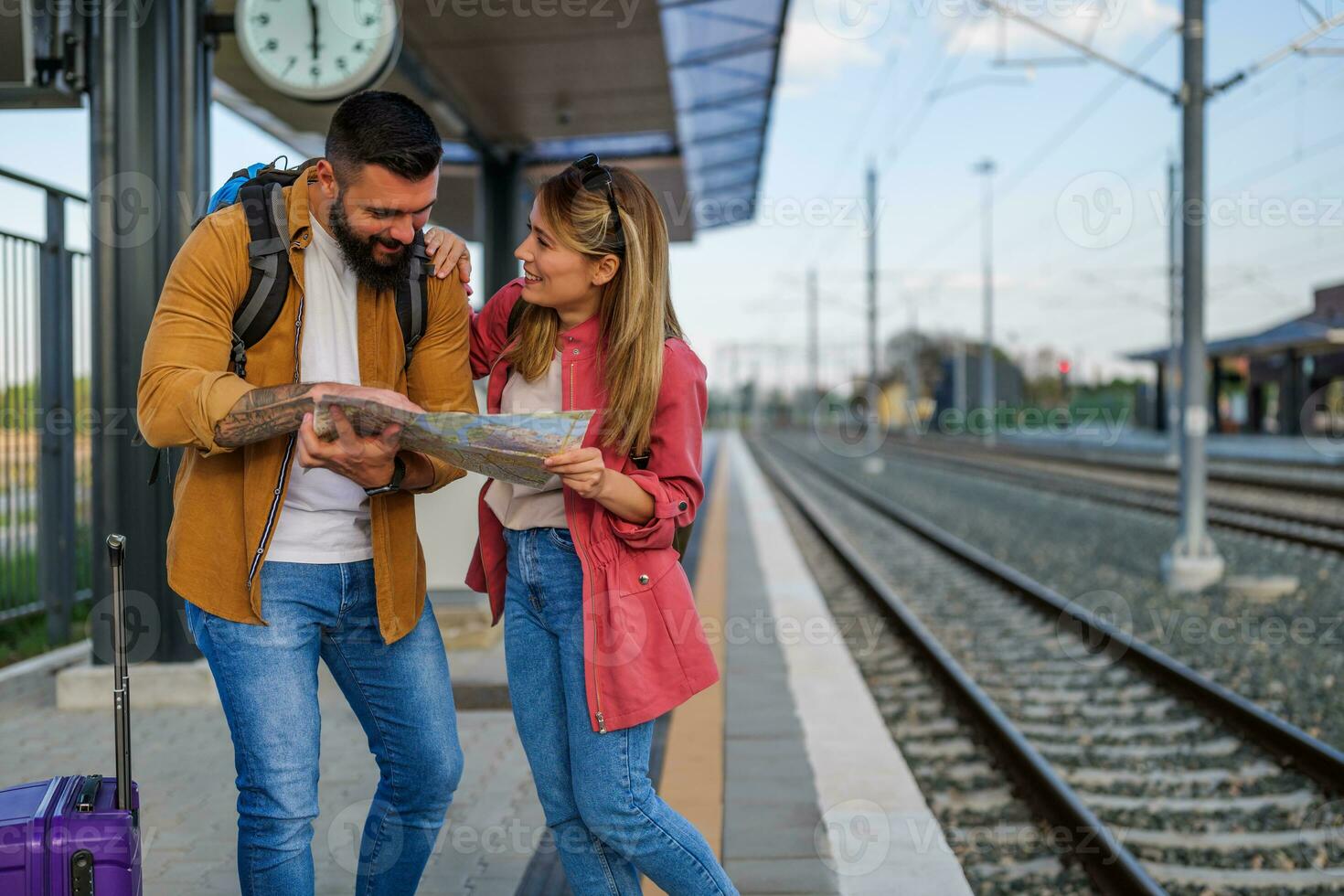 gelukkig paar is staand Bij spoorweg station en aan het wachten voor aankomst van hun trein. ze zijn op zoek Bij kaart. foto