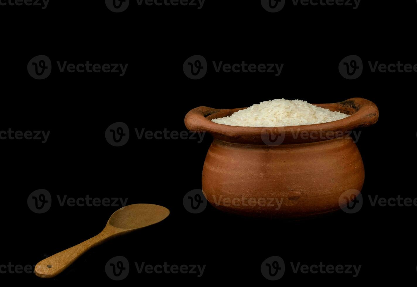 jasmijn rijst in een aarden pot en een houten pollepel geïsoleerd op een zwarte achtergrond foto