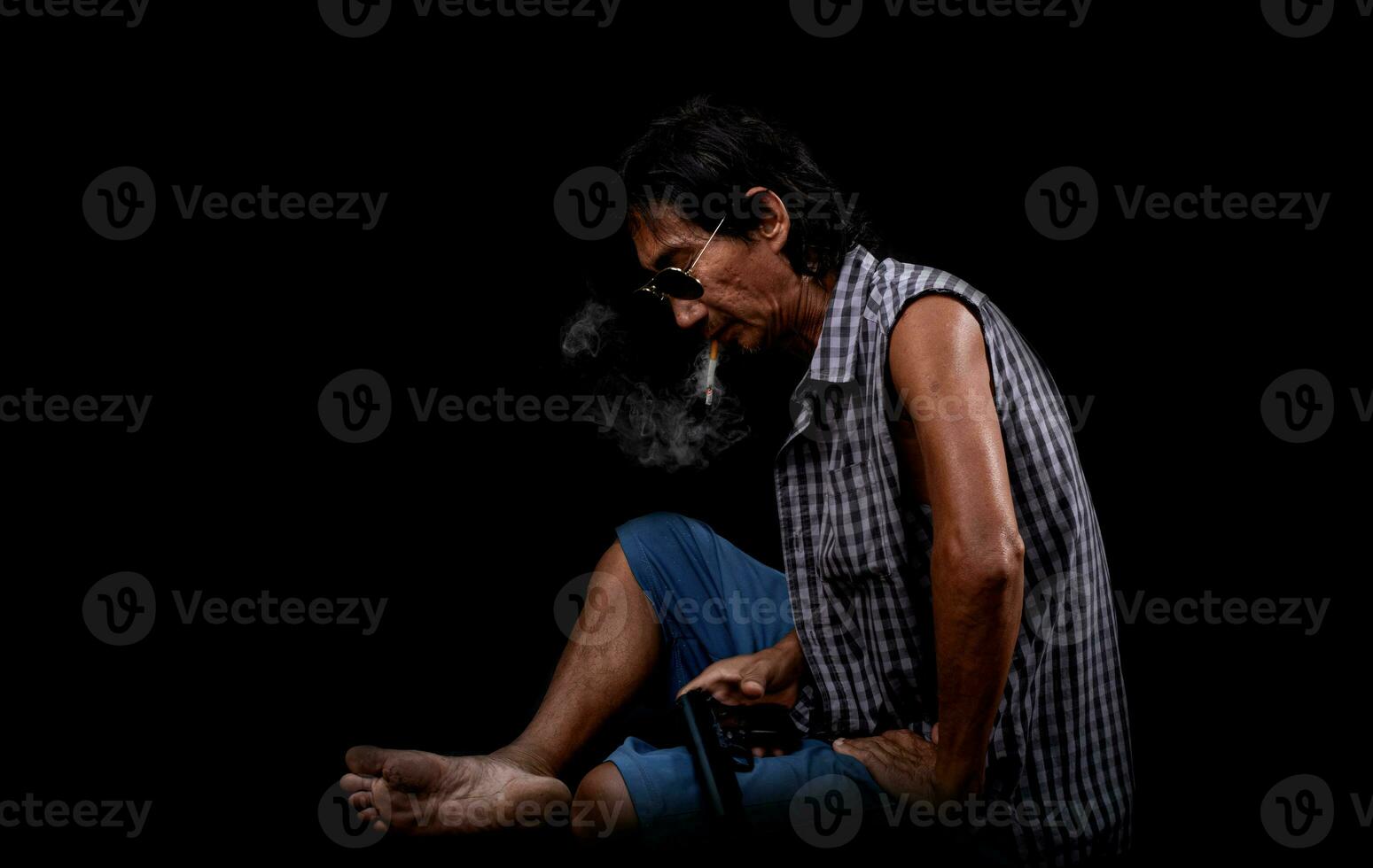 portret slanke oude Aziatische man roken en met een pistool op een zwarte achtergrond foto