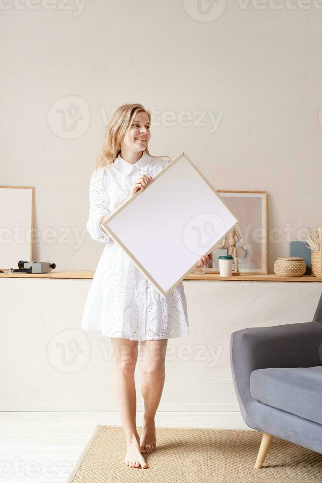 vrouw in jurk Holding blanco kader in leven kamer foto