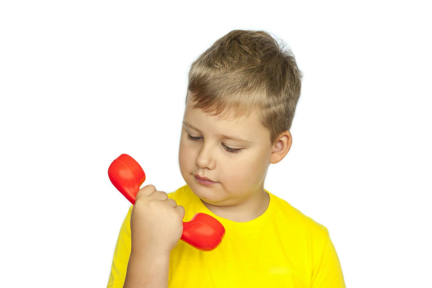 een jongen in een geel t-shirt Aan een wit achtergrond met een rood telefoon ontvanger. de concept van een banier met informatie. ruimte voor de tekst. foto