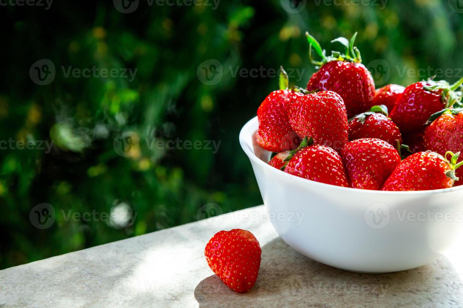 rode rijpe aardbeien in een witte kom met groene natuur achtergrond foto