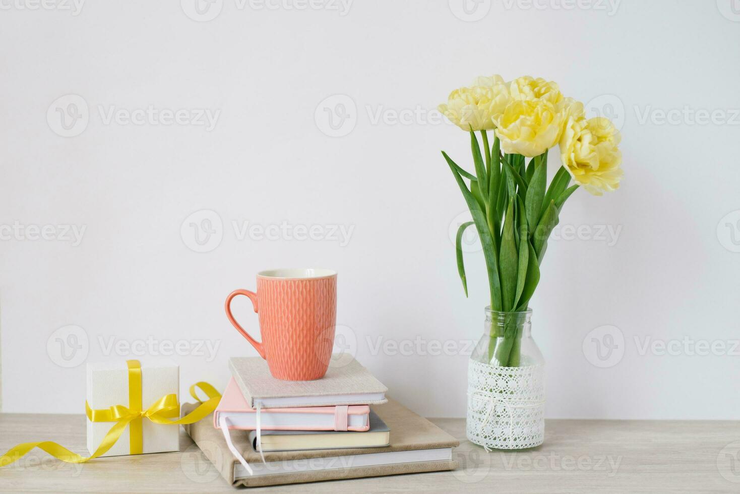 een mok, een veel van blocnotes in een stapel, een boeket van geel voorjaar tulpen en een geschenk doos Aan de bureaublad van een freelancer of blogger vrouw. vrouwen dag, Valentijnsdag dag of verjaardag. voorkant keer bekeken foto
