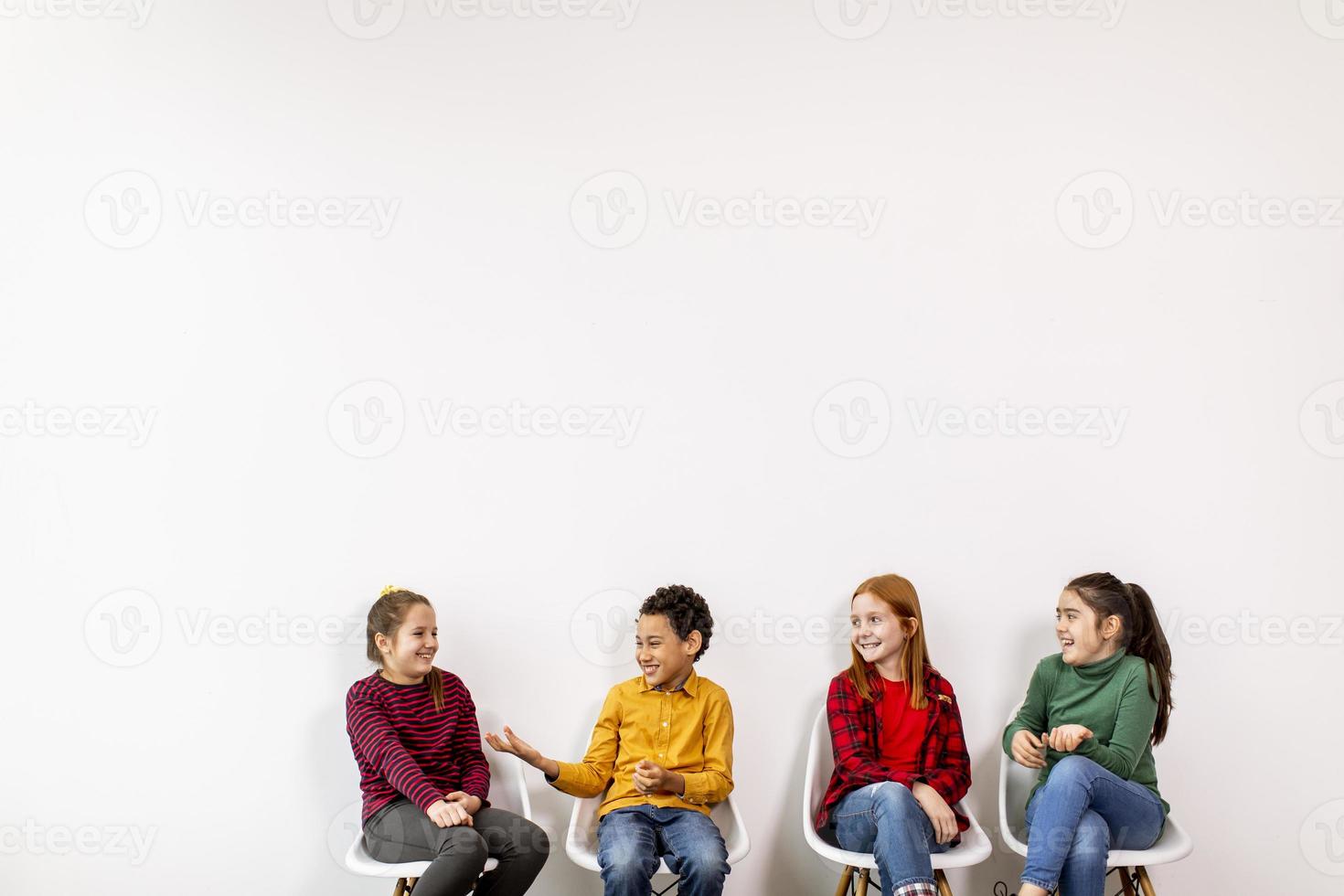 portret van schattige kleine kinderen in spijkerbroek zittend in stoelen tegen witte muur foto