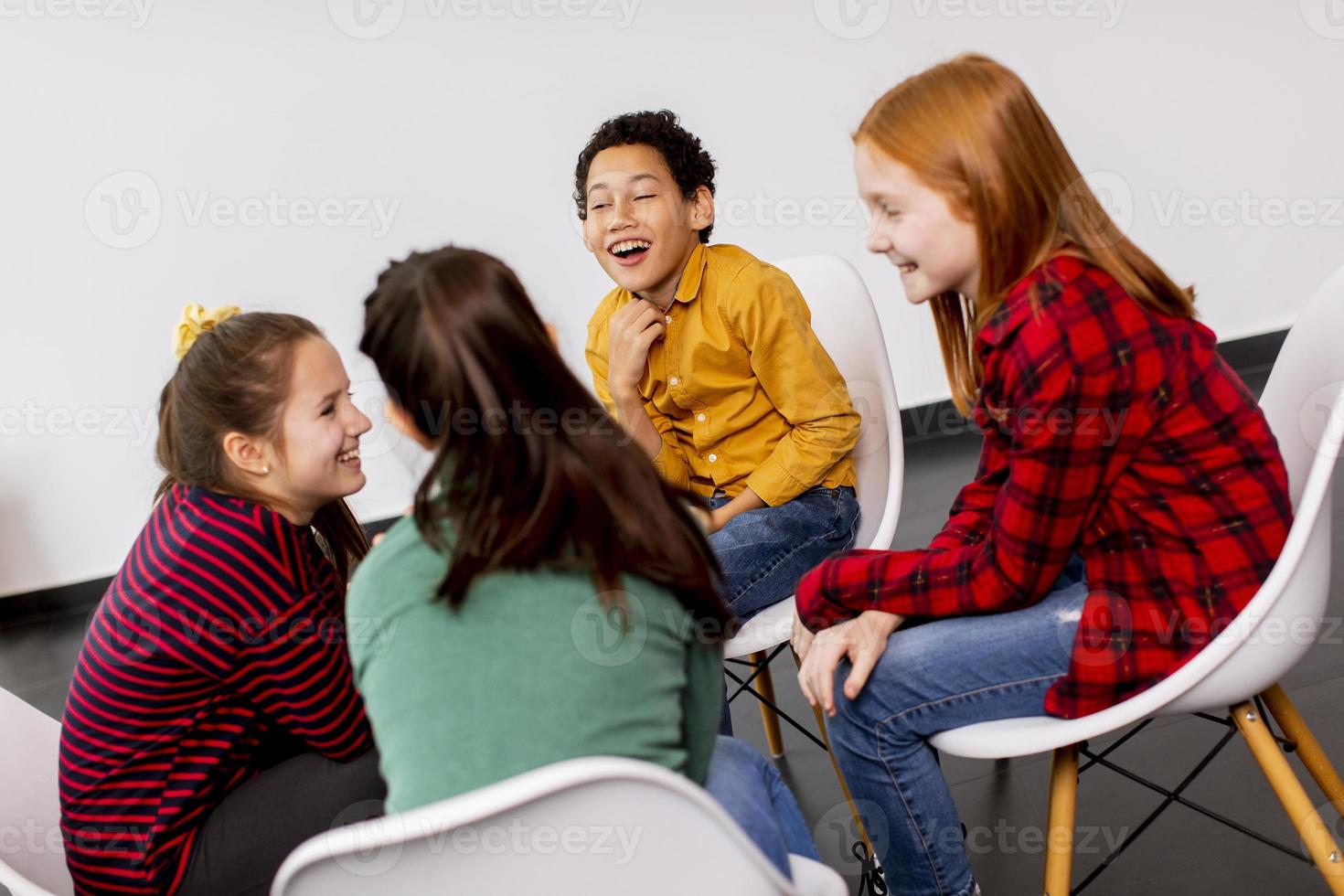 portret van schattige kleine kinderen in spijkerbroek praten en zitten in stoelen tegen witte muur foto