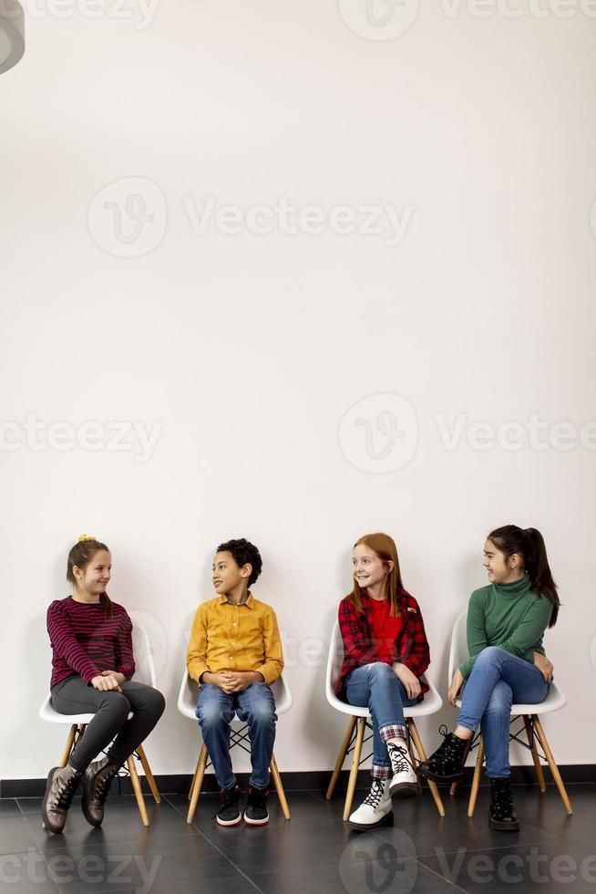 portret van schattige kleine kinderen in spijkerbroek zittend in stoelen tegen witte muur foto