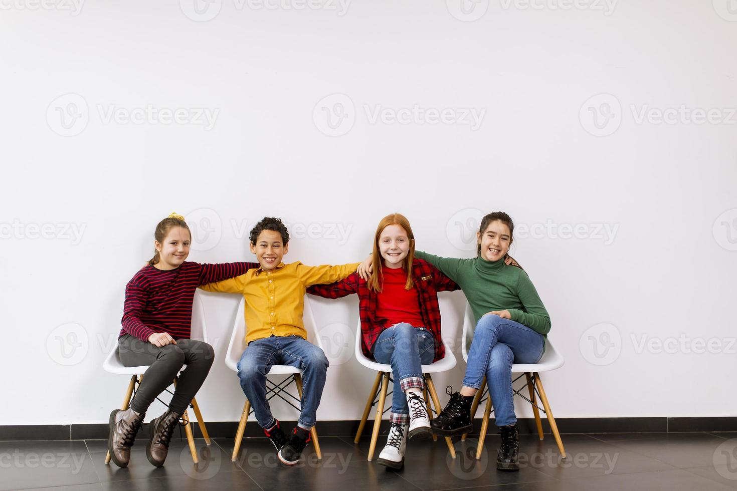 portret van schattige kleine kinderen in spijkerbroek zittend in stoelen tegen witte muur foto