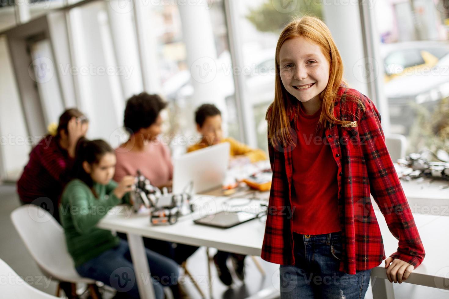 schattig klein meisje staan voor kinderen programmeren van elektrisch speelgoed en robots op robotica klas foto