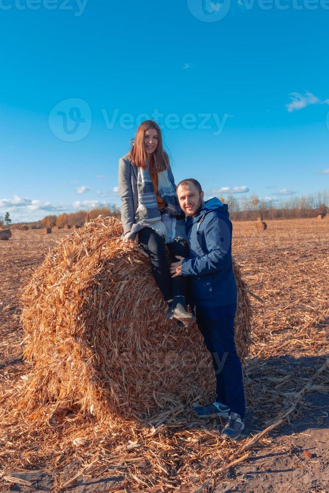 een meisje en een jongen staan in de buurt van een grote baal met hooi in een veld en een blauwe lucht foto