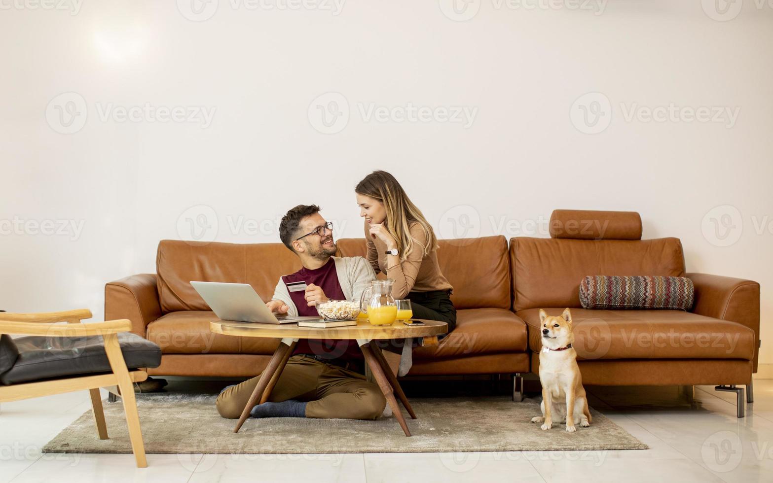 jonge vrouw en jonge man met behulp van laptop voor online betaling zittend op de bank met hun shiba inu-hond thuis foto