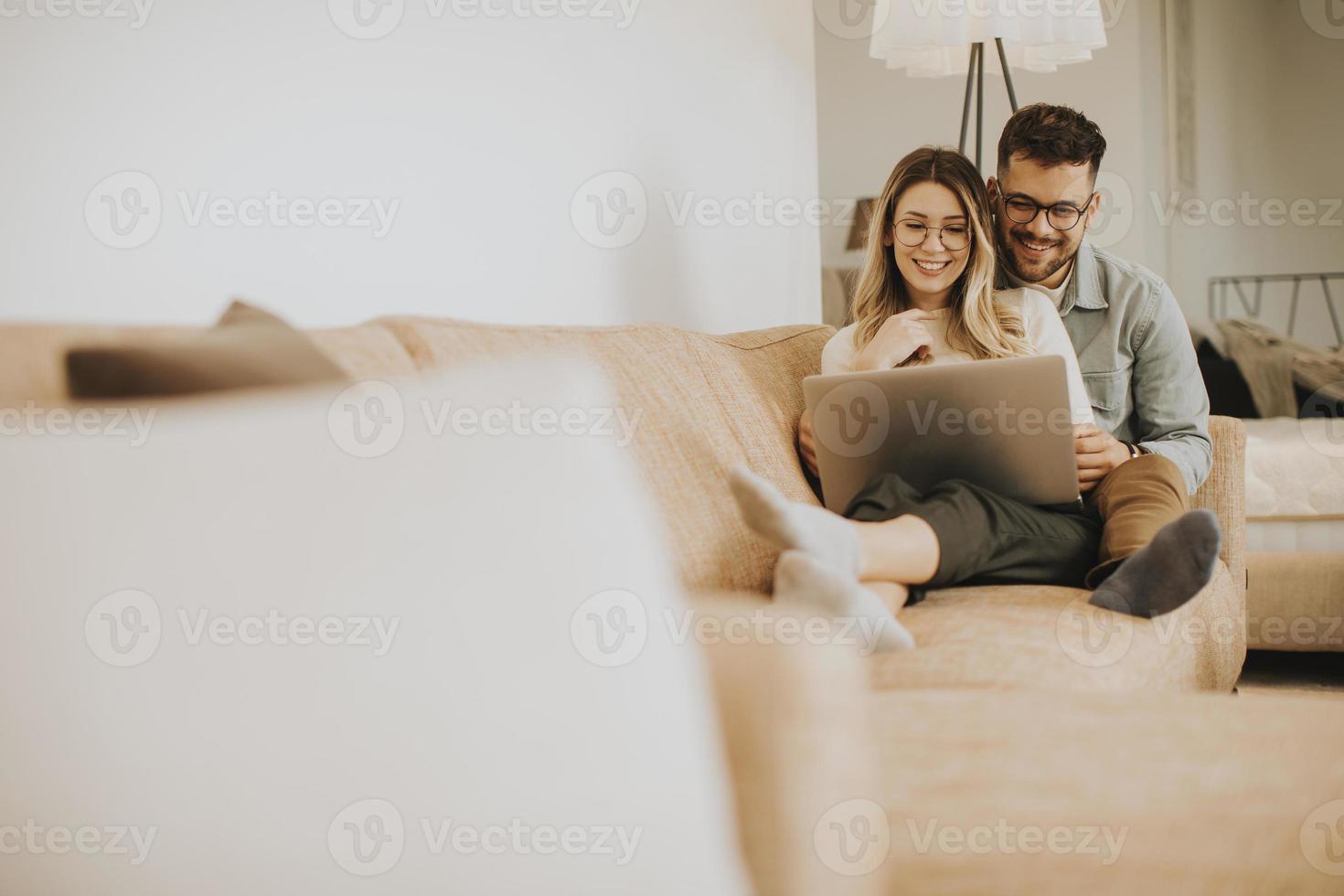 jong koppel samen met behulp van laptop zittend op de bank thuis foto