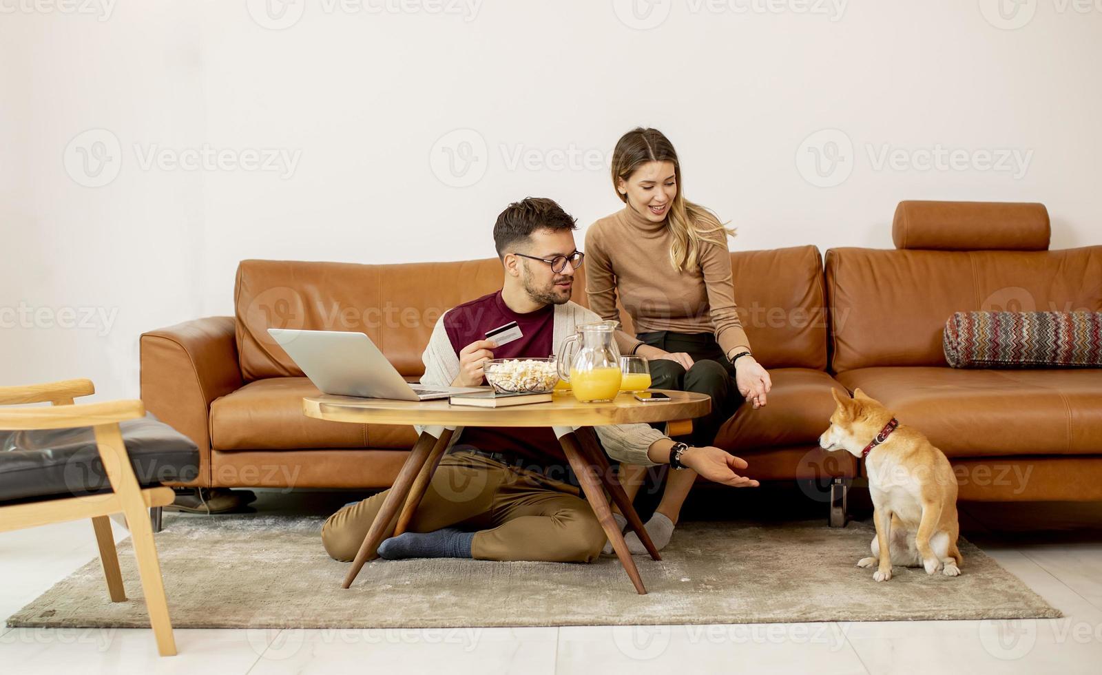 jonge vrouw en jonge man met behulp van laptop voor online betaling zittend op de bank met hun shiba inu-hond thuis foto