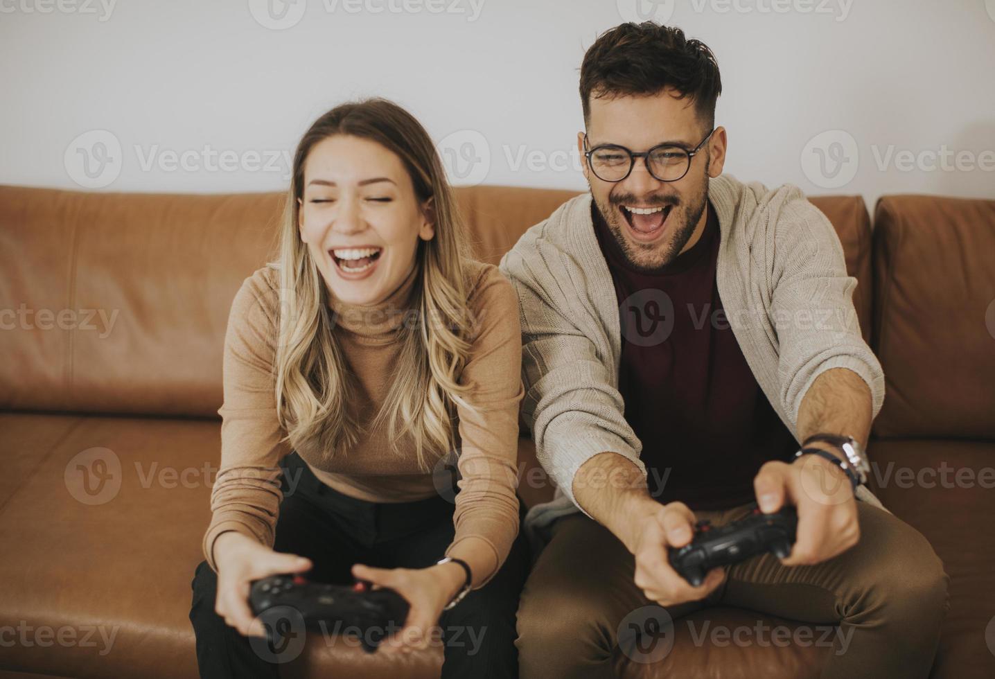 jong koppel spelen van videogames thuis zittend op de bank en genieten foto