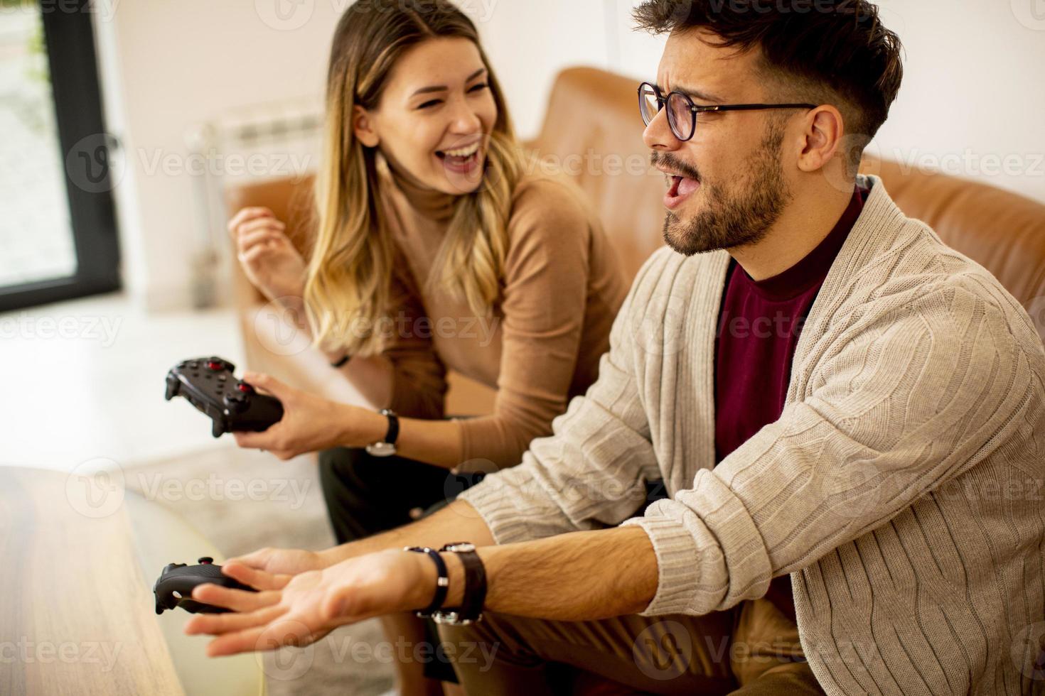 jong koppel spelen van videogames thuis zittend op de bank en genieten foto