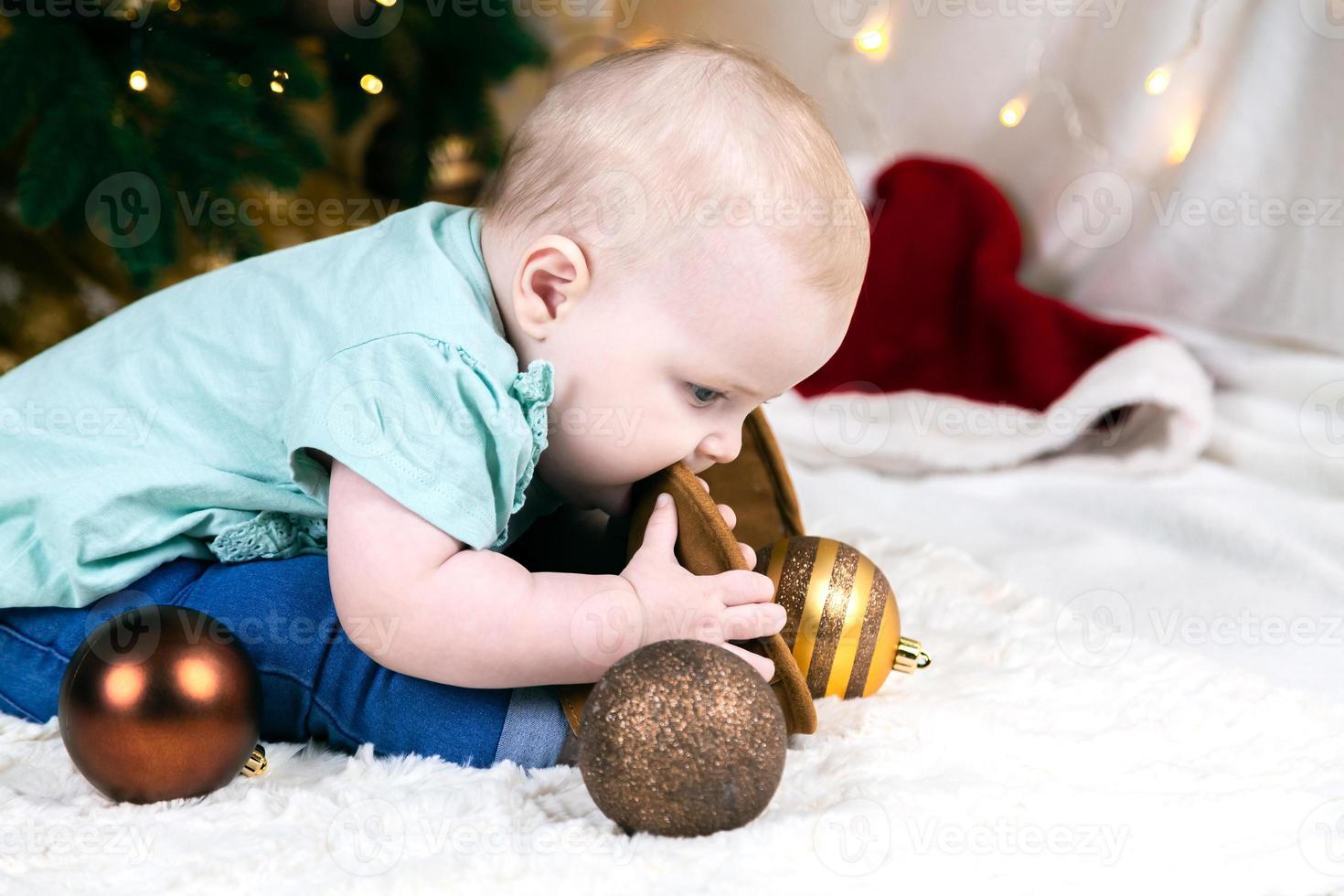 baby in jeans en schoenen zit in de buurt van een kerstboom foto