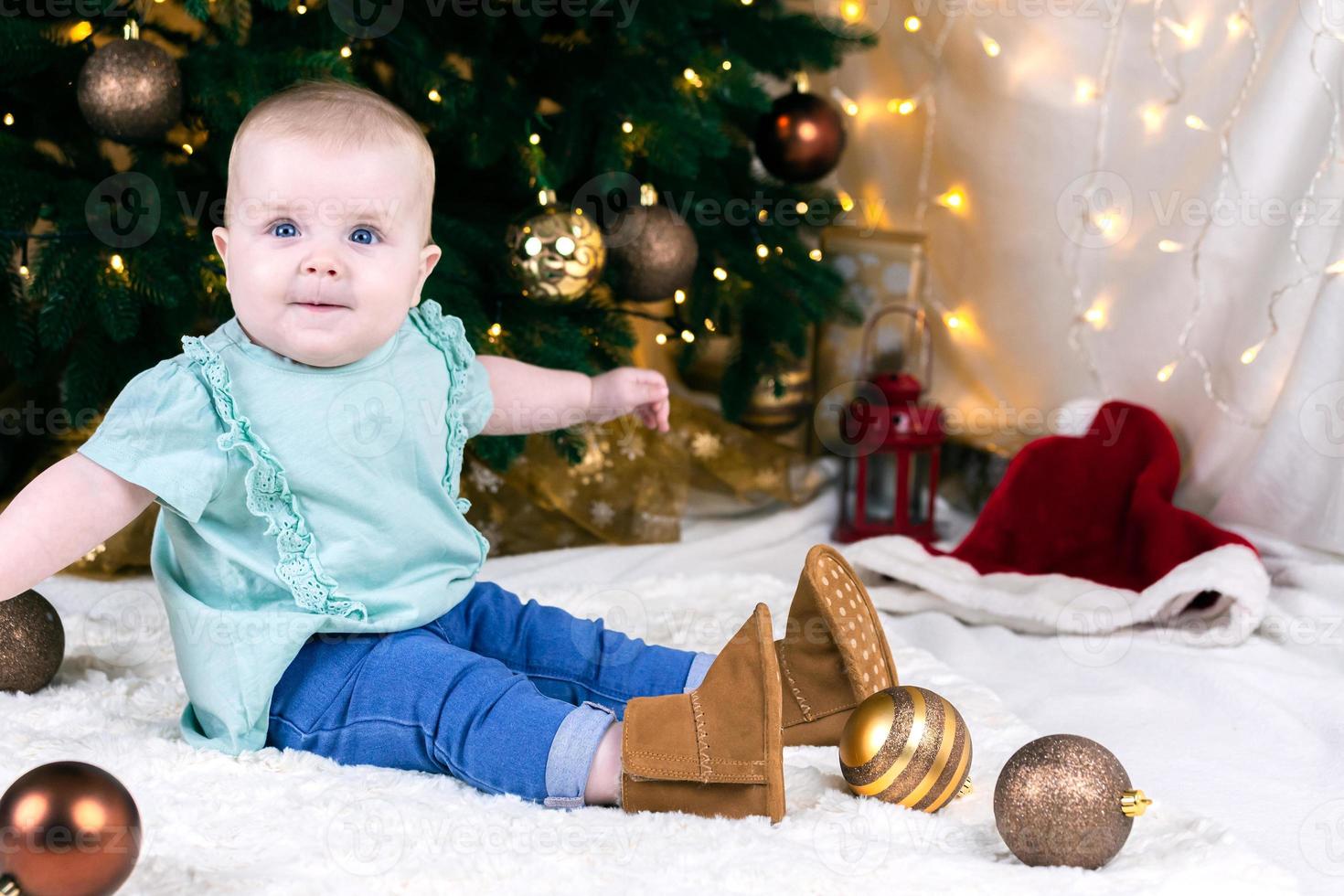 baby in jeans en schoenen zit in de buurt van een kerstboom foto