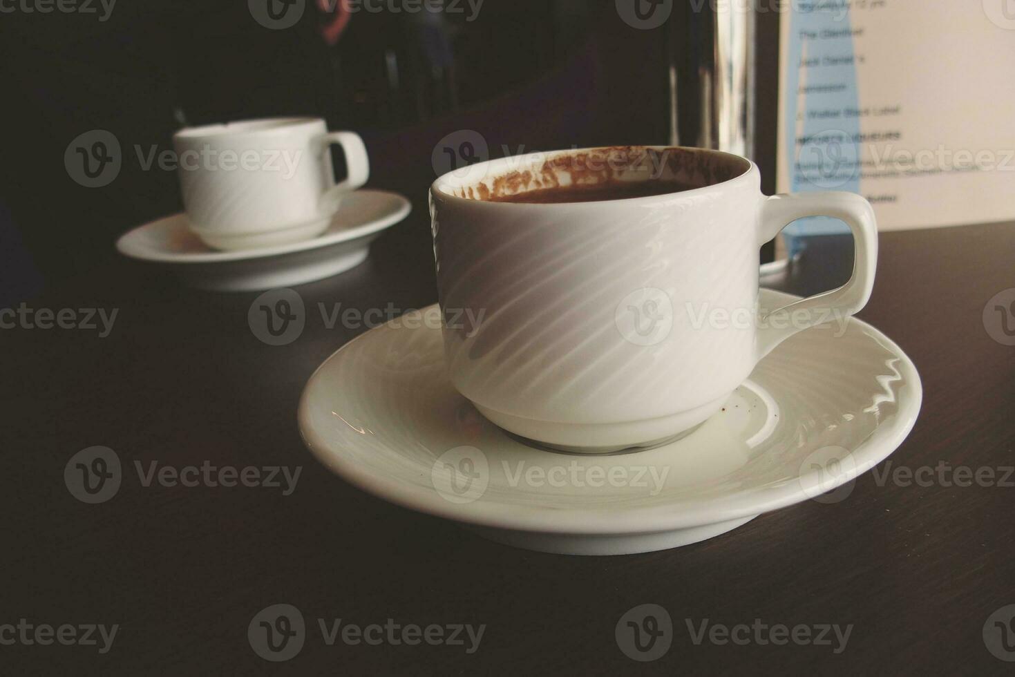 weinig wit kop met heet zwart koffie Aan een bruin tafel foto