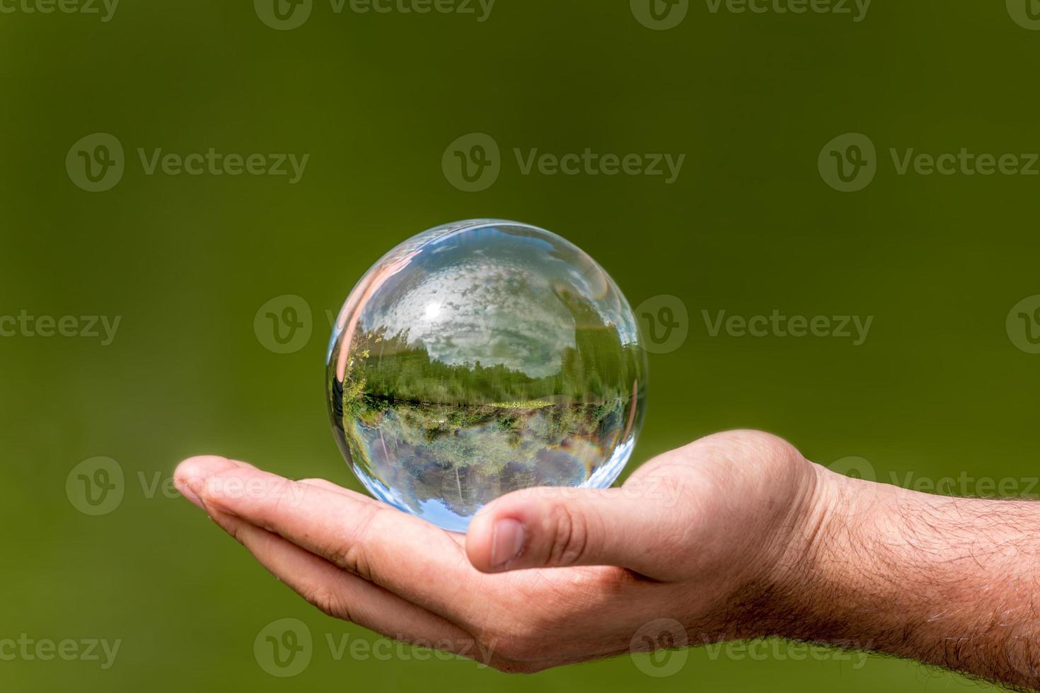 glazen bol met gespiegelde meerbomen en lucht ligt in één hand tegen groene achtergrond foto