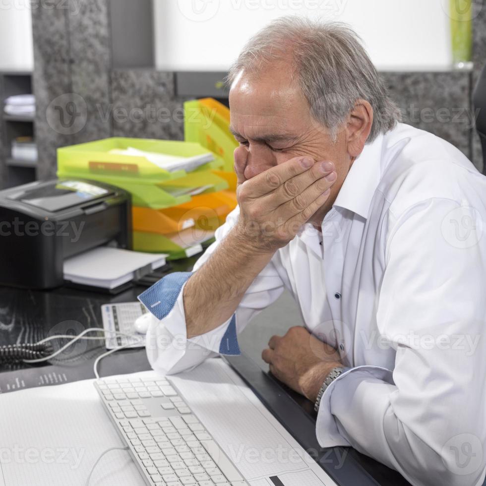 senior man zit wanhopig achter een bureau foto