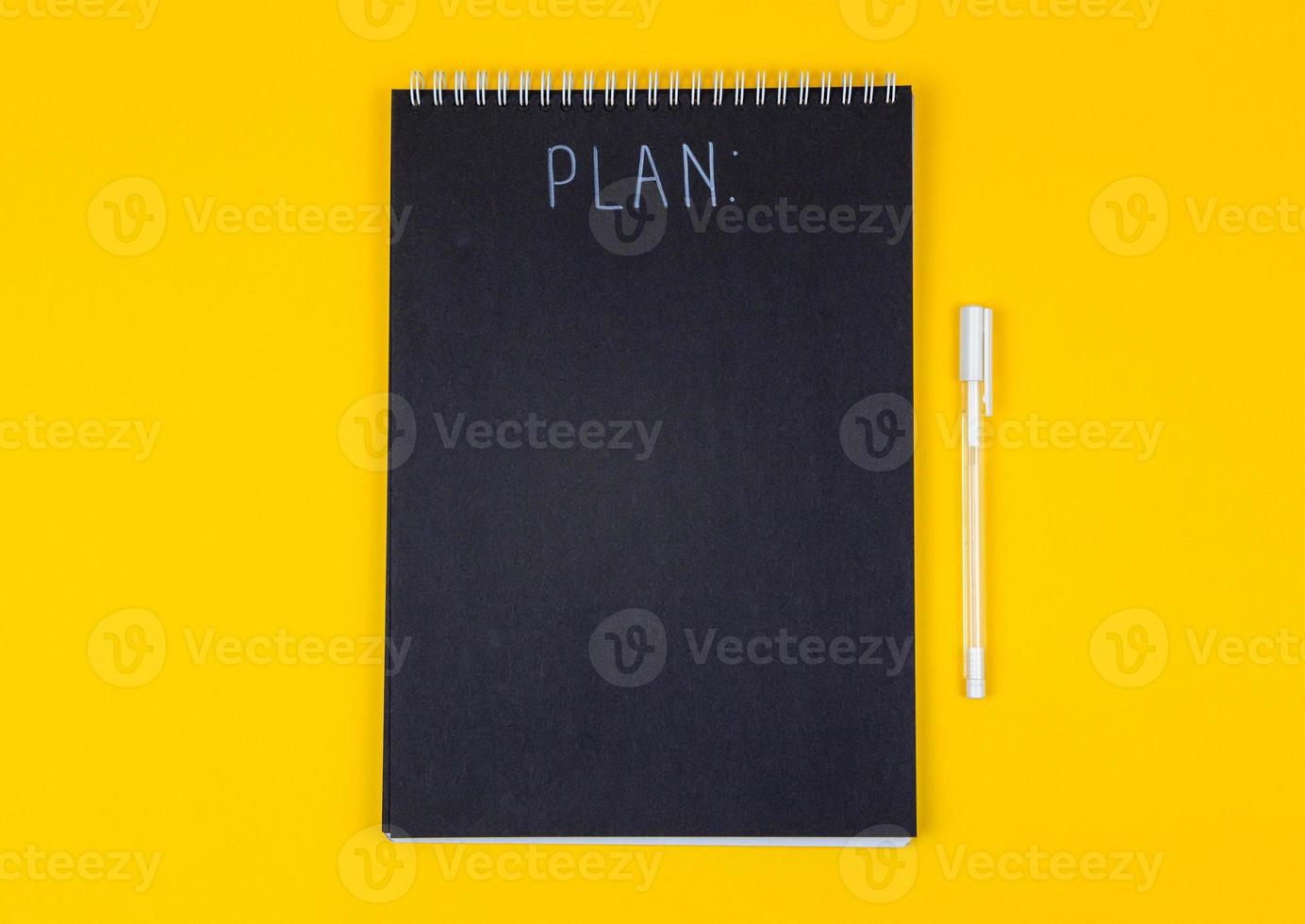 lege zwarte spiraal notitieblok en witte marker met kalligrafische inscriptie van het woord plan op gele achtergrond foto