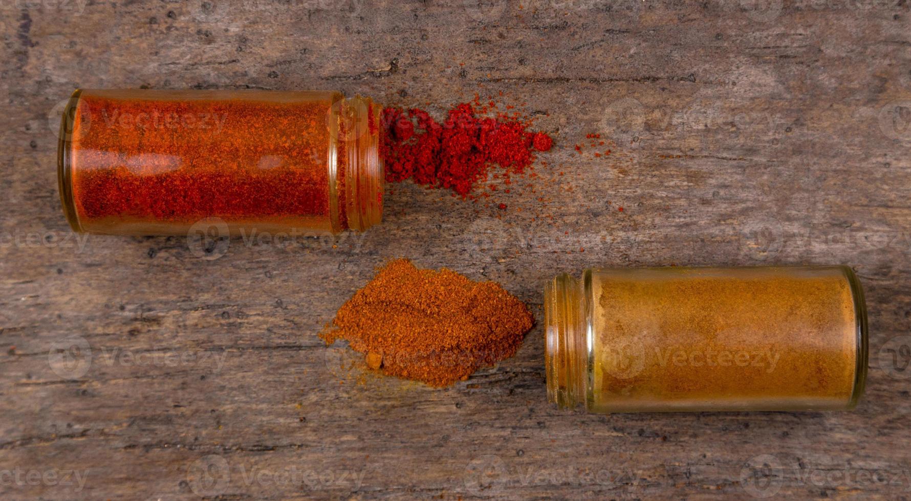 Spaanse peper kleurrijke poeder kruiden verspreid van fles op houten achtergrond foto