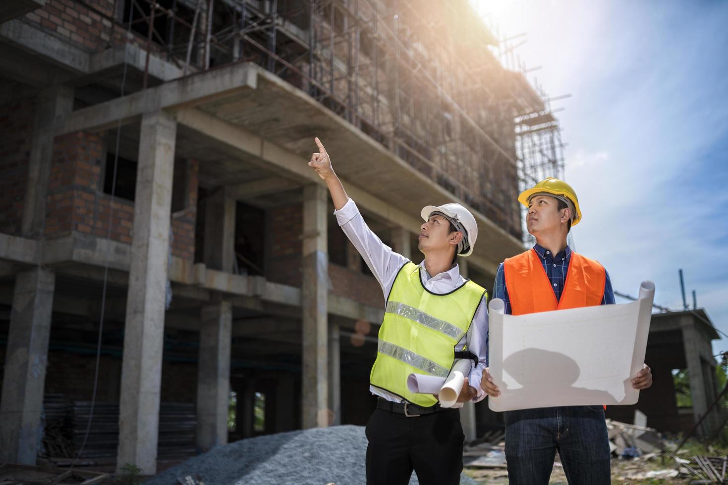 zakenman en ingenieur kijken naar de blauwdruk van een gebouw op een bouwplaats voor hoogbouw foto