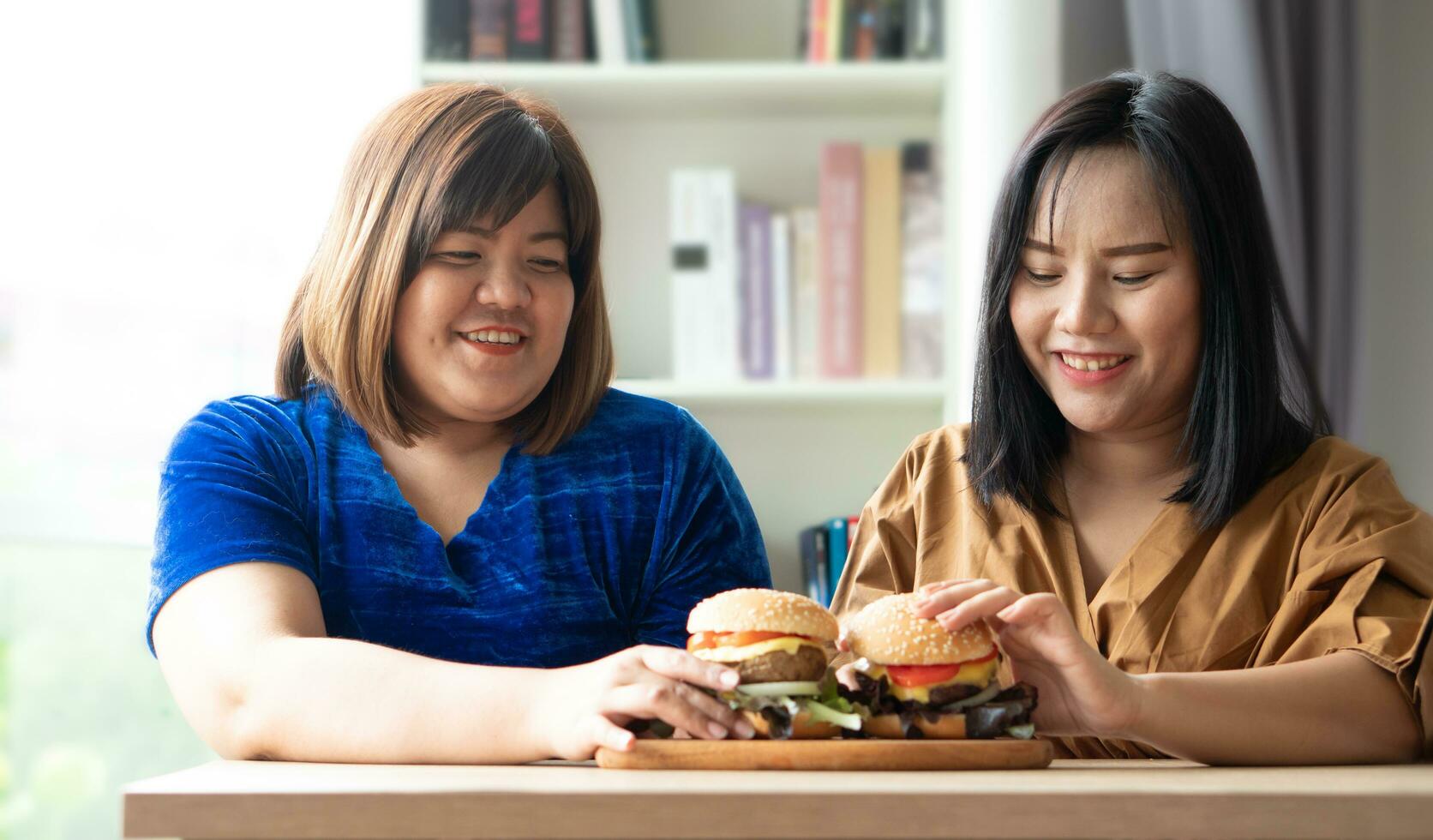 hongerig te zwaar vrouw Holding Hamburger Aan een houten bord, gedurende werk van huis, krijgen gewicht probleem. concept van eetbui aan het eten wanorde bed foto