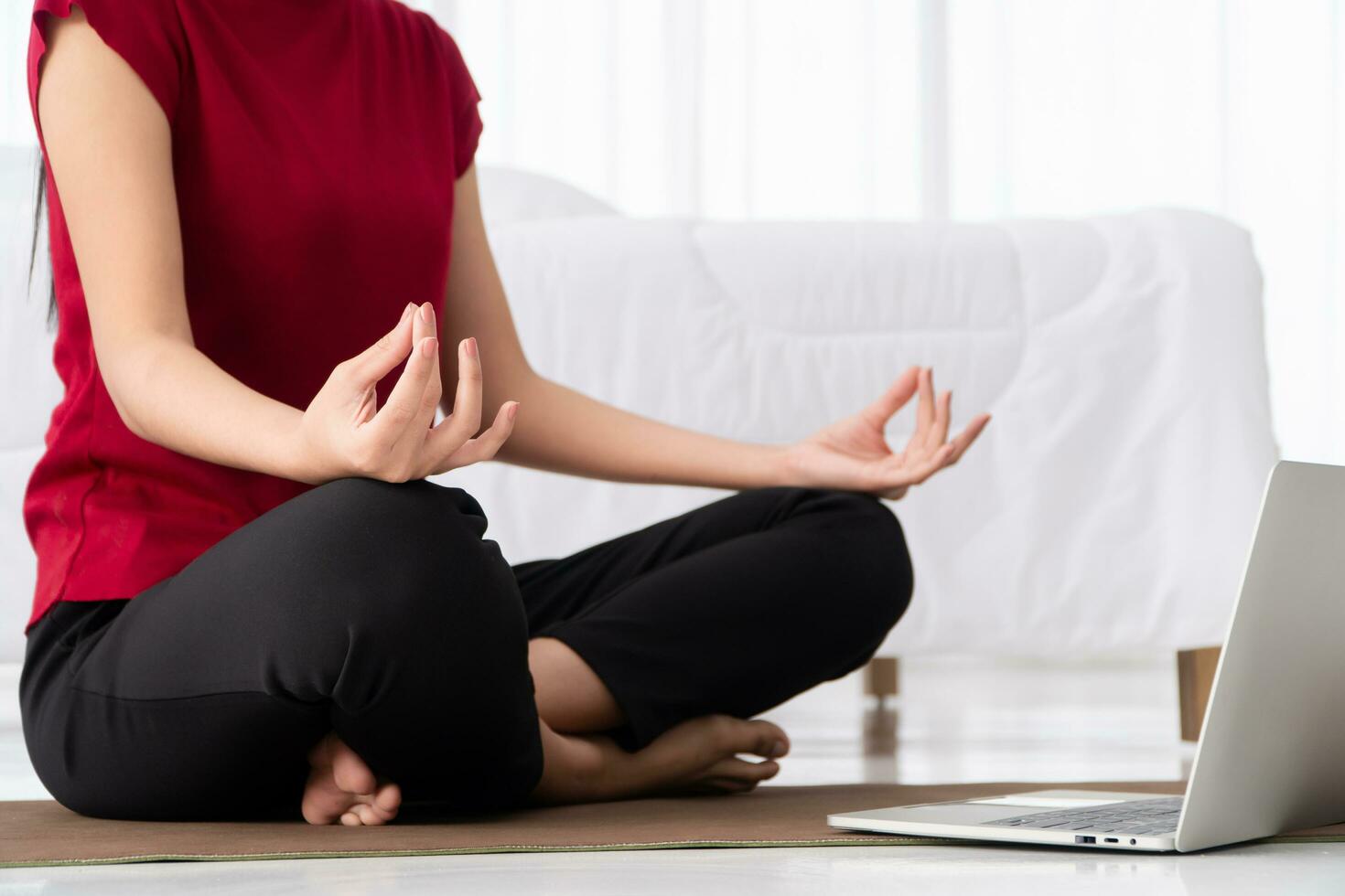 portret van gezonde jonge aziatische vrouw die yoga-oefeningen beoefent die in de slaapkamer zitten en thuis online op laptop leren. concept van lichaamsbeweging en ontspanning, technologie voor een nieuwe normale levensstijl foto