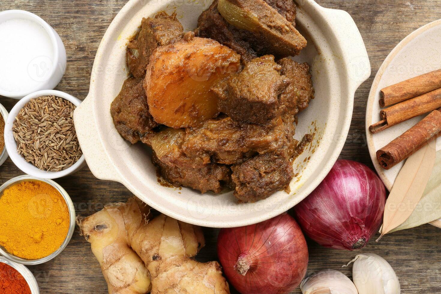 rundvlees bhuna droog kerrie met aardappel in keramisch kom ingrediënten chili komijn koriander kurkuma aangedreven zout ui knoflook gember baai blad kaneel kardemom kruidnagel over- rustiek hout achtergrond foto