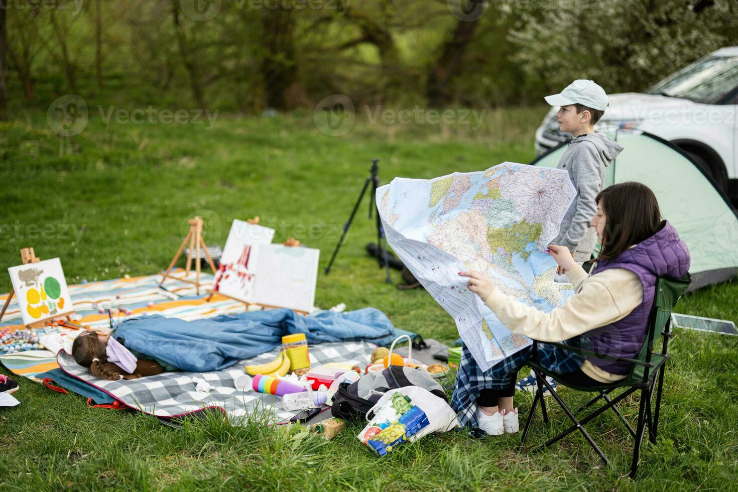 moeder houden Europa kaart, met kinderen zitten Aan stoel tegen auto Aan picknick. foto