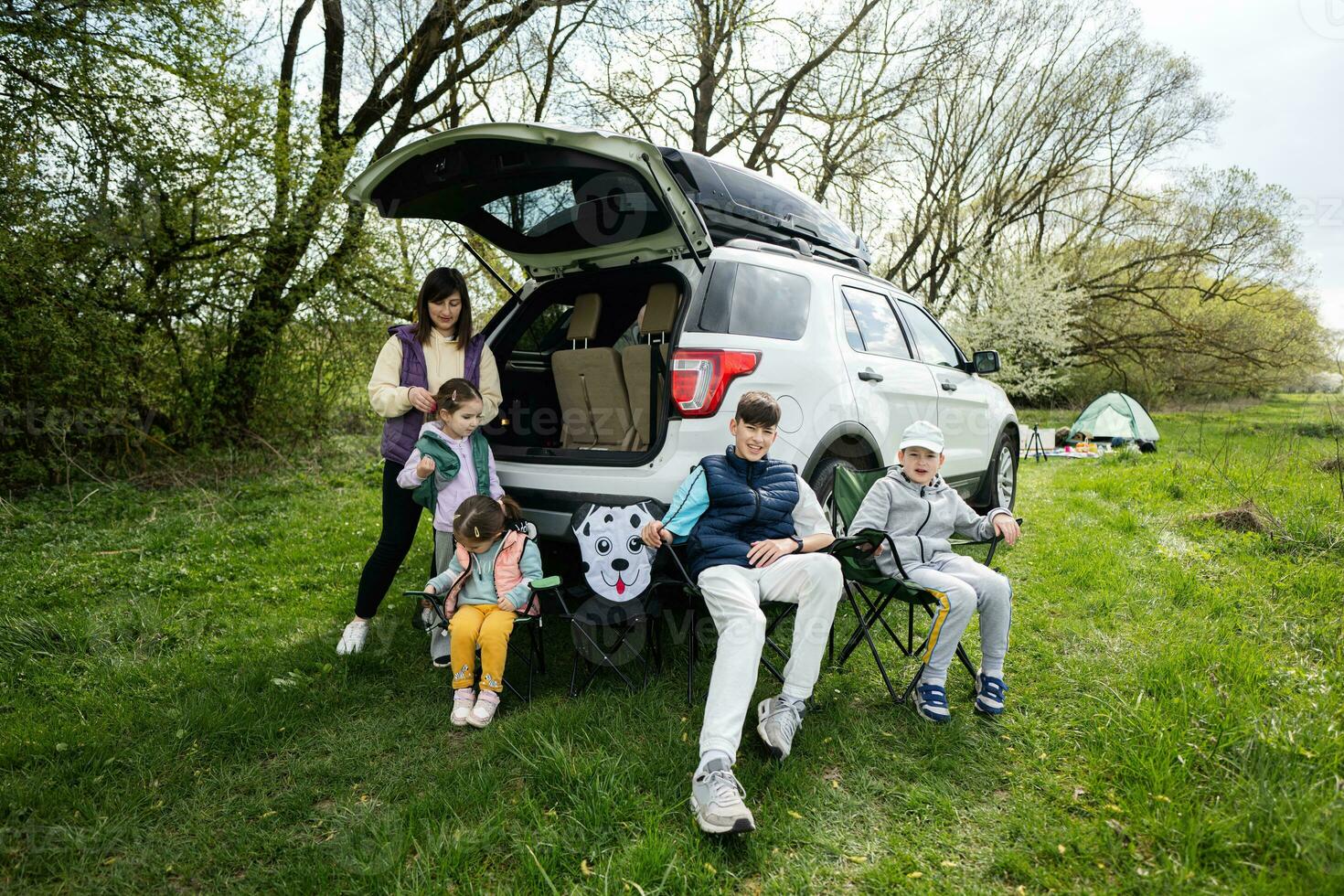 moeder met kinderen zitten Aan stoel tegen auto Aan picknick. foto