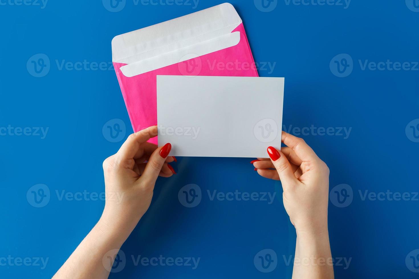 roze envelop met een lege kaart in handen op een blauwe achtergrond foto