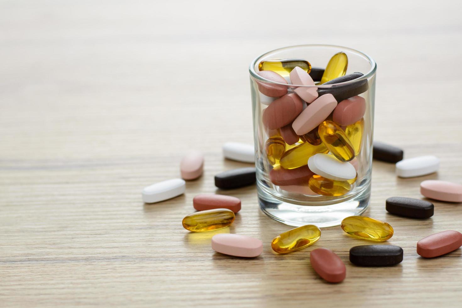 visolie capsules en multivitamine supplementen in het kleine glas op de houten tafel met kopie ruimte foto