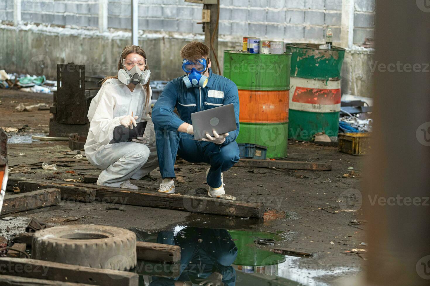 noodgeval verontreiniging fabriek concept. ingenieurs vervelend monteur jumpsuits en ppe en gas- maskers inspecteren olie Aan de fabriek vloer. foto