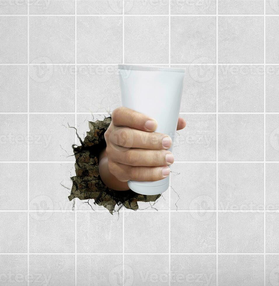 menselijk hand- Holding een schoonheidsmiddelen fles door de muur met scheuren foto