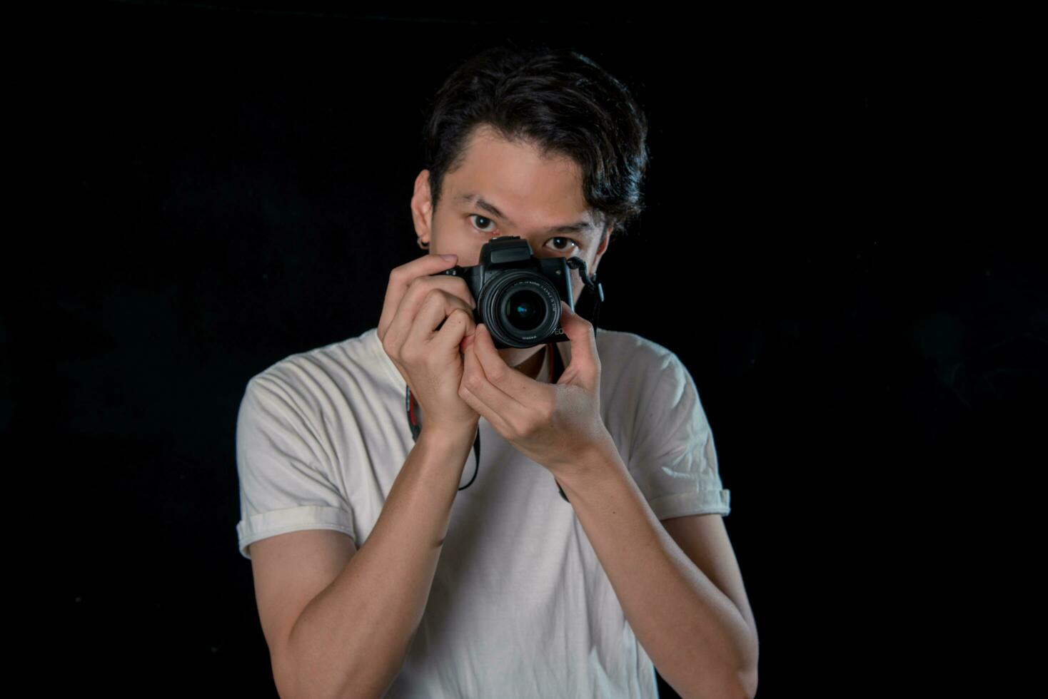 portret van mannen Holding een dslr op zoek camera Aan donker studio achtergrond , Aziatisch foto