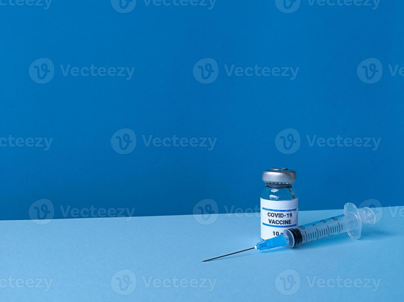 medische fles met covid 19-vaccin en spuit op blauwe achtergrond met gekantelde trendy skyline en kopieerruimte foto