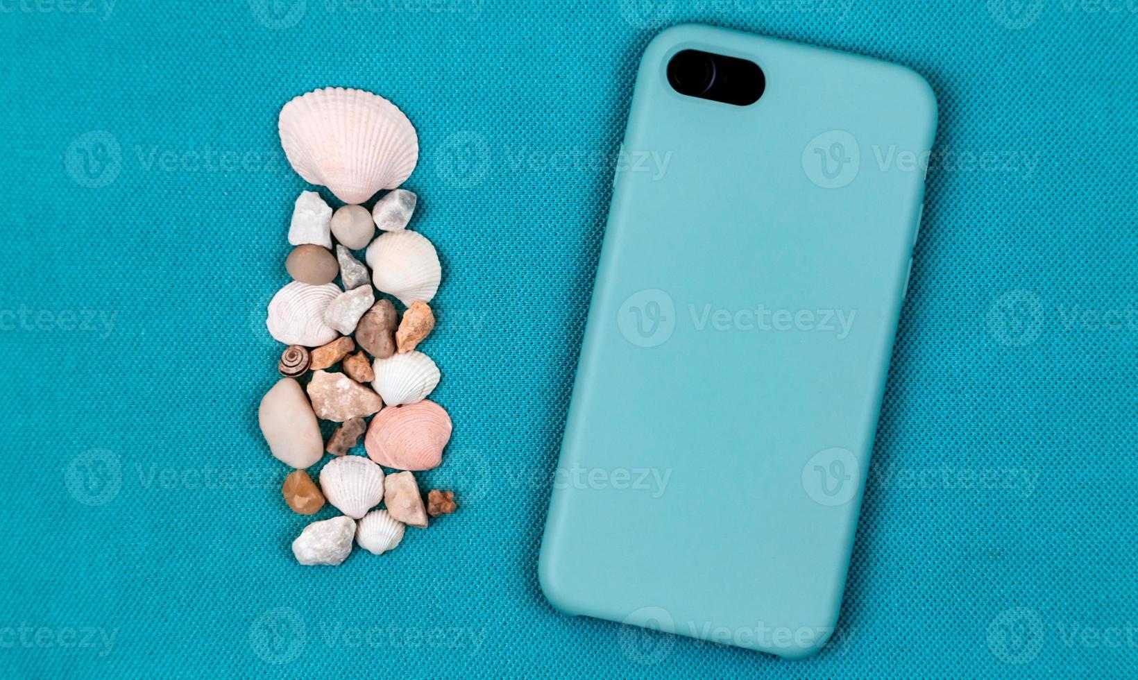 achterkant van smartphone in aqua blauw hoesje op een trendy aquaachtergrond met zeeshells foto