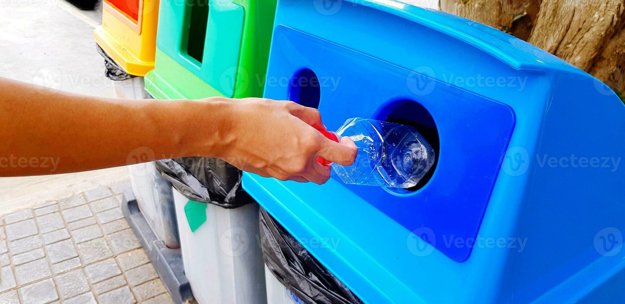 dichtbij omhoog vrouw hand- Holding en dumping plastic fles van water in blauw recycle bak, prullenbak of afval. schoonmaak Oppervlakte en recycling gebruikt met kopiëren ruimte. foto