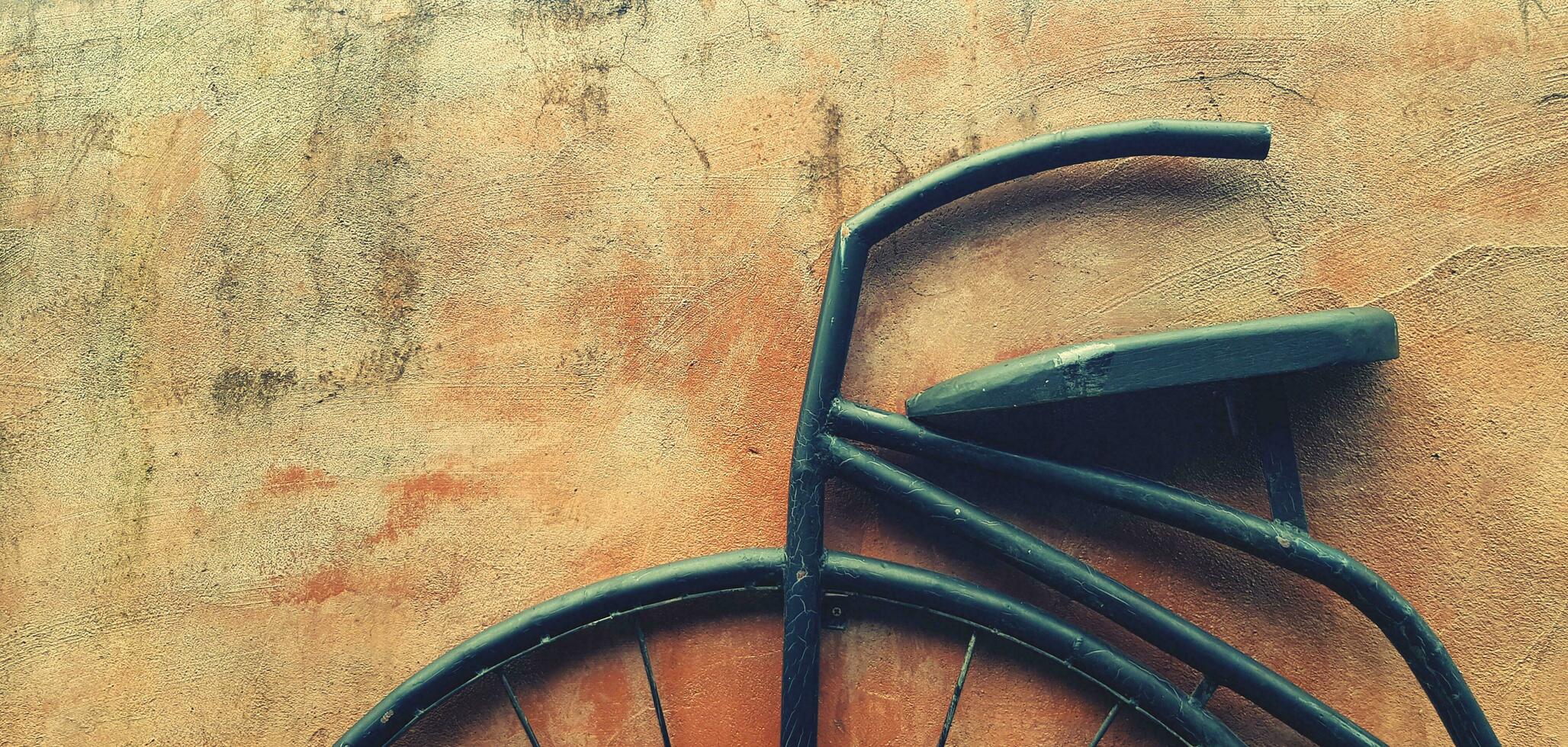 groot zwart retro staal fiets wiel met omgaan met en stoel voor rijden geïsoleerd Aan oranje of bruin grunge muur met kopiëren ruimte in wijnoogst toon foto