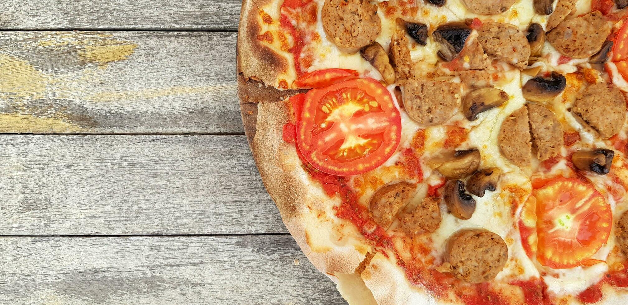 peperoni pizza Aan grunge grijs houten achtergrond of tafel met links kopiëren ruimte. Koken ingrediënt met tomaat, paddestoel en Thais worst. deze voedsel gebakken door gebruik houtskool fornuis. foto