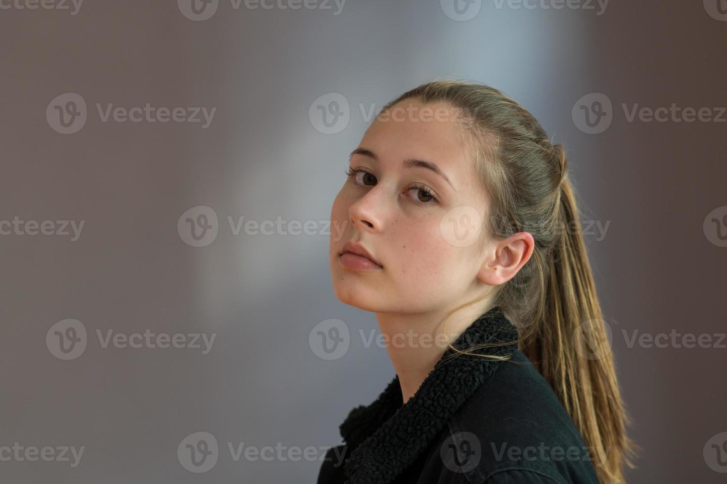 driekwart schot of semi profiel portret van een mooi tienermeisje met paardenstaart haar poseren kijken naar de camera op een grijze achtergrond foto