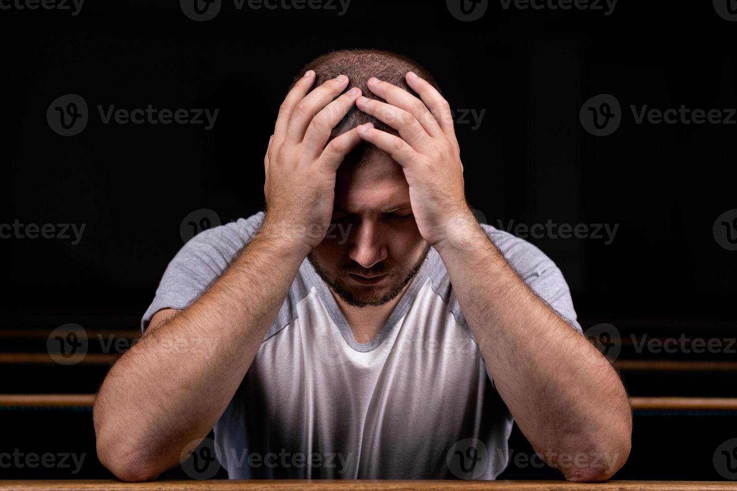 een trieste christelijke man in wit overhemd zit met nederig hart in de kerk te bidden foto