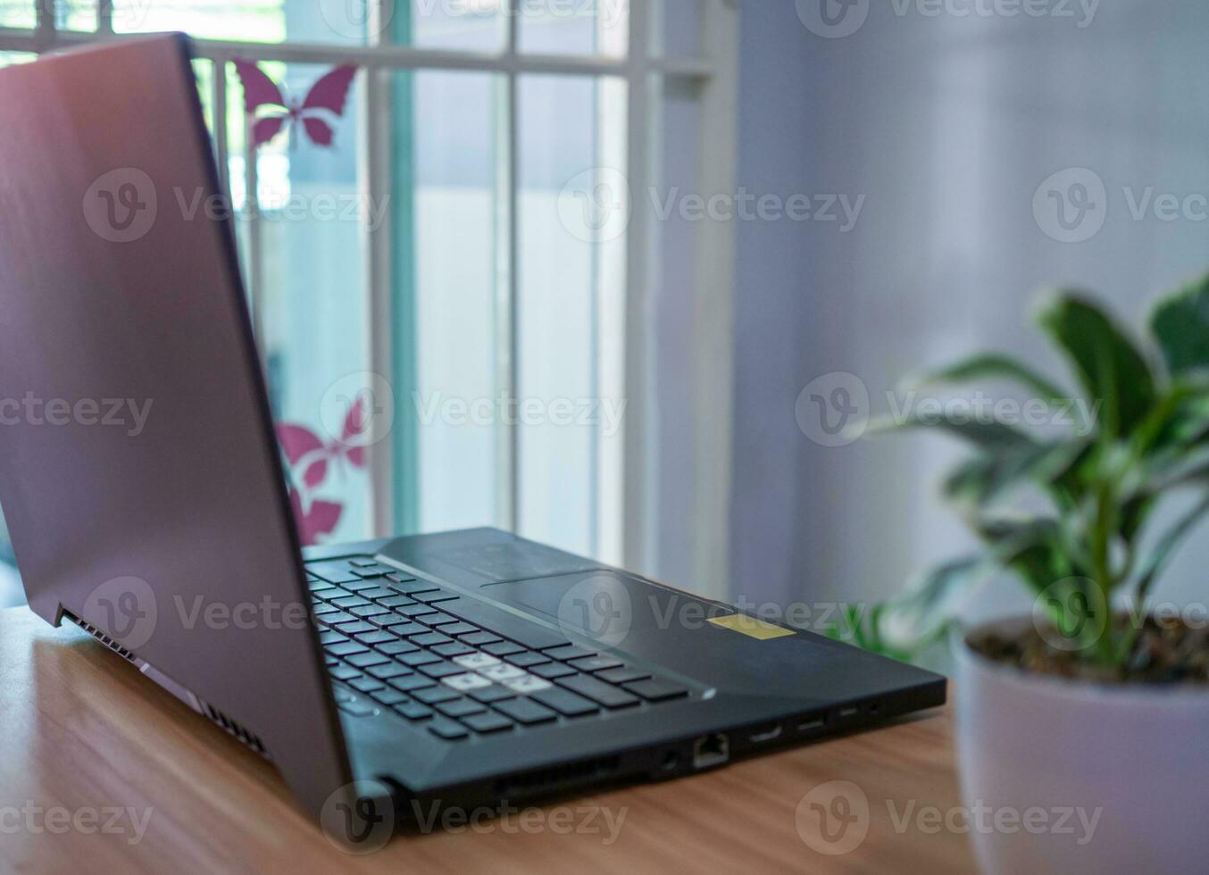 achterzijde visie van laptop computer Aan houten tafel met venster wazig achtergrond en planten in modern kamer foto