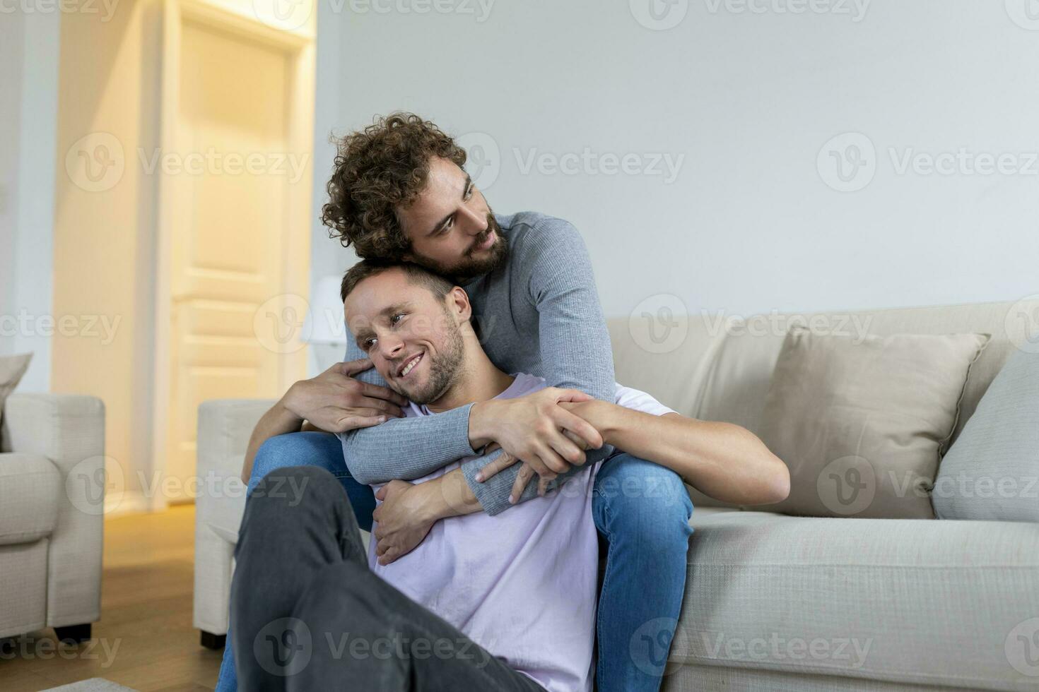 lief homo paar zoenen terwijl zittend in hun leven kamer Bij huis. twee romantisch jong mannetje geliefden hebben pret binnenshuis. jong homo paar leven samen. foto